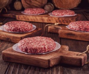 Raw,Hamburgers,On,Cutting,Board,With,Wood,Pile,Background